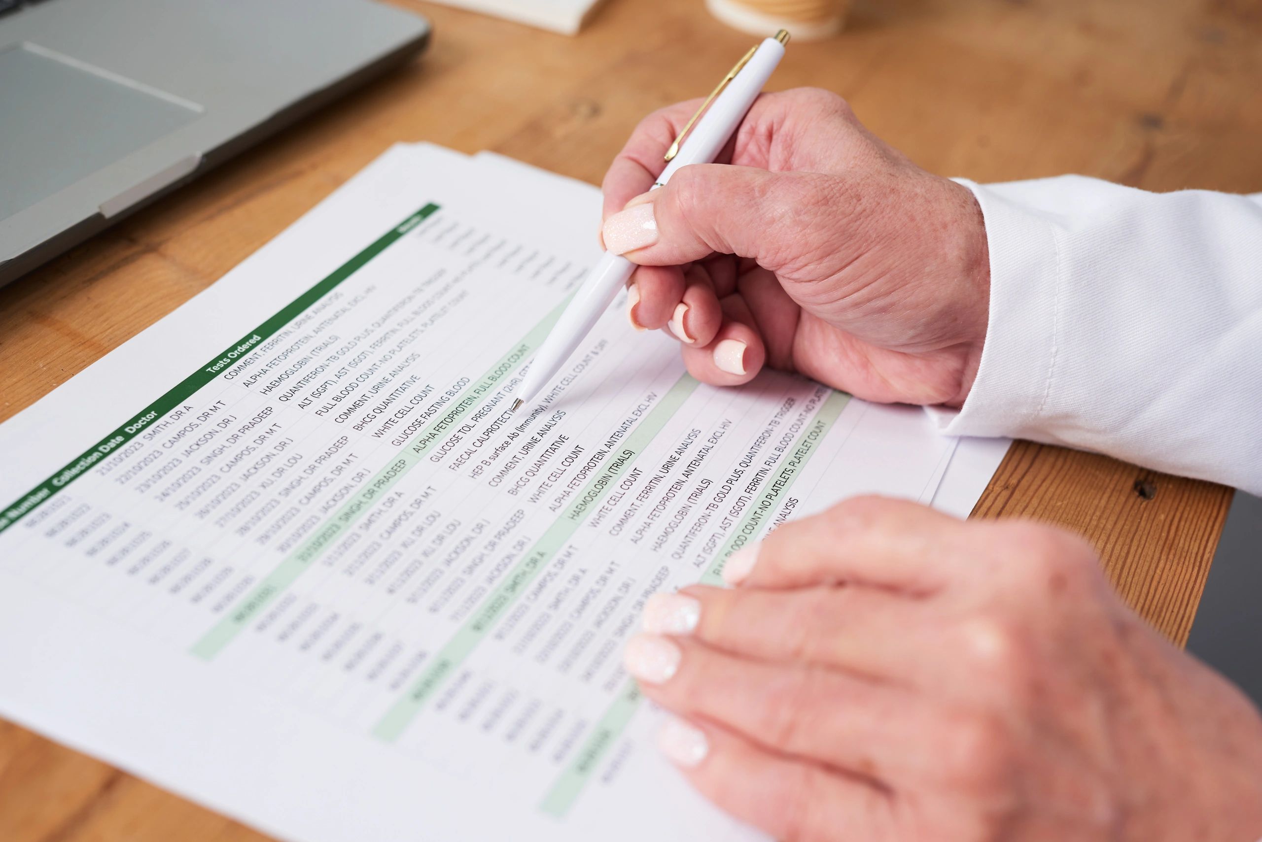 Hand signing a reviewed document next to a laptop